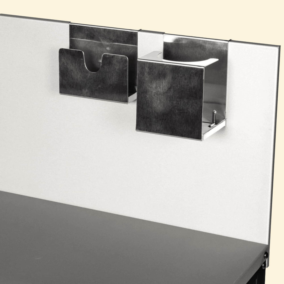 Supports inox fixés sur une crédence de cuisine extérieure, comprenant un porte-ustensiles ouvert et un rangement rectangulaire fermé, vus en gros plan sur fond clair.