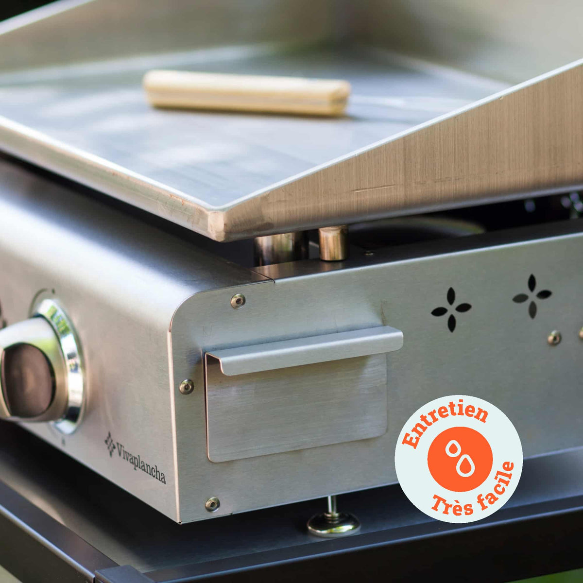 Gros plan sur la plancha Vivaplancha montrant le récupérateur de graisse en inox et un outil de nettoyage posé sur la plaque, avec un badge “Entretien très facile”.