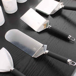 Ensemble de spatules en inox avec manches noirs, disposées sur un plan de travail en bois foncé, montrées en vue rapprochée.